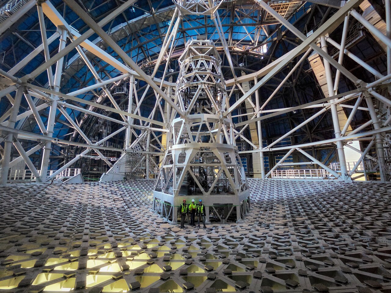 Looking almost like an optical illusion, today’s Picture of the Week highlights why ESO’s Extremely Large Telescope (ELT) is called that. This image was taken inside the telescope’s dome, with some of the ELT’s team standing above the massive structure that will hold its main mirror. This 39-metre-diameter reflective surface will comprise 798 mirror segments that will work together as a single mirror, in what will be the biggest optical telescope on Earth. This photo was taken when the ELT construction reached a momentous milestone. For the first time, the telescope’s structure was rotated around its vertical axis. ESO staff at the construction site, together with Ace/Cimolai’s team, who are leading the construction of the dome and main structure, rotated the telescope first by hand by a few centimetres, and then a full rotation using auxiliary motors. While this may seem small, the entire structure currently weighs around 3500 tonnes, which will further increase up to 4600 tonnes once the mirrors and science instruments are installed. The structure rests on a layer of oil just 80 microns thin that allows the telescope to rotate smoothly. Testing this motion is thus key to ensuring that this massive telescope can point at all areas of the southern sky. “For me, this is a beautiful reminder of what can be achieved when people push in the same direction, literally and figuratively,” says Roberto Tamai, the ELT’s Programme Manager at ESO, shown on the right in this image. Marco Sciarra, Executive President of Cimolai, stands in the centre with Pascal Martinez, ESO Project Manager for the Dome and Main Structure, to the left. The ELT, expected for first light later this decade, will be a gamechanger in astronomical research, as the world’s ‘biggest eye on the sky’. Besides its exceptional size, its cutting-edge instruments will allow us to understand our Universe better than ever before. Link  Video of the ELT rotation test